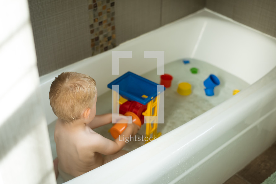 a toddler boy playing in the bathtub 