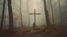 Monk prays near a wooden cross in the foggy day