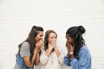 Friends laughing together standing against a white brick wall. 