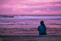 a young woman sitting on a beach at sunset 