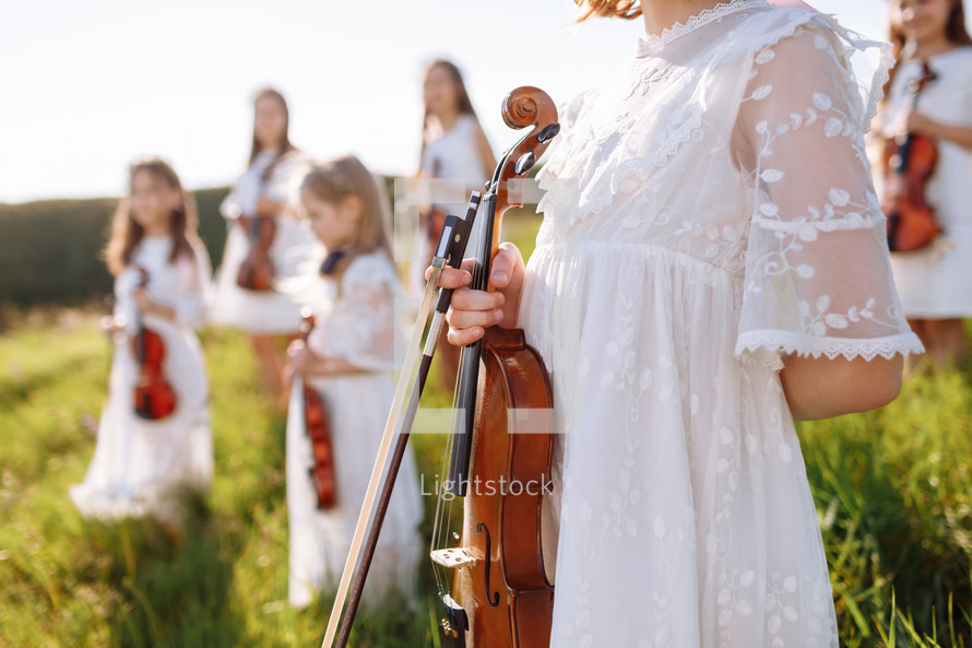 Group of young violinists playing with an orchestra band at an outdoor during the summer festival. Profile face and instrument. Image with selective focus.