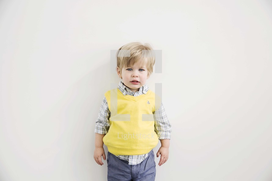 portrait of a young boy in church clothes against white wall.