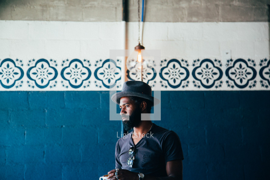 African American man standing in front of a blue wall holding a coffee cup