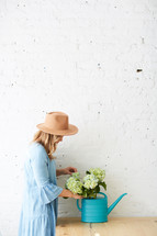 a woman arranging hydrangeas in a watering can on a table 