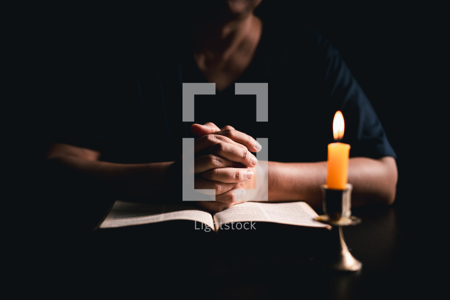 Bible and candlelight with praying hands