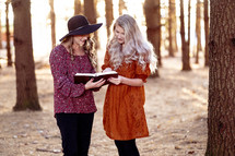 two women reading a Bible outdoors in the woods in autumn 