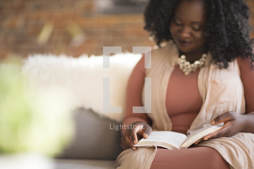 A woman sitting on a couch reading a Bible