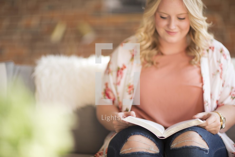 a woman siting on a couch reading a Bible 