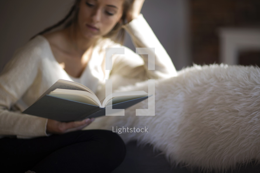 a woman sitting on a couch reading a Bible in the sunlight 