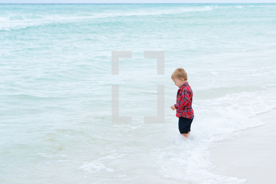 a toddler with his feet in the ocean 