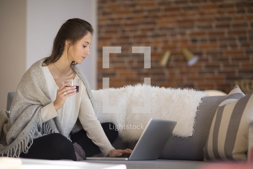 a woman sitting on a couch with a blanket on her lap working on a laptop computer 