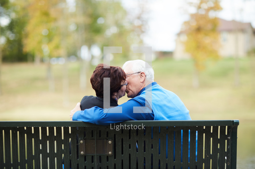 elderly couple kissing on a park bench 