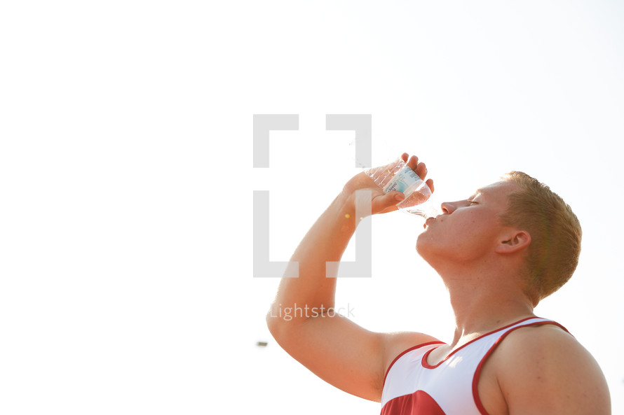 man drinking from a water bottle at sports practice 
