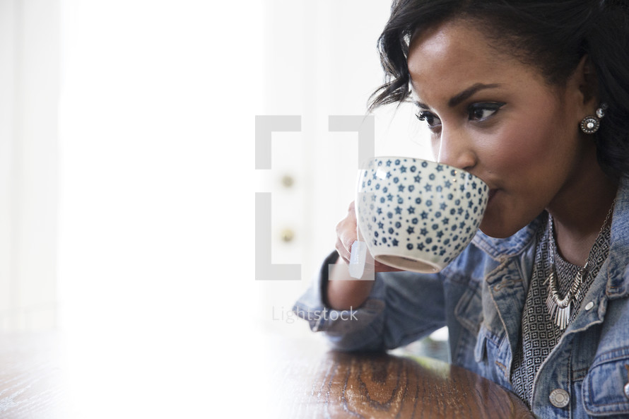an African American woman sitting at a table sipping coffee 