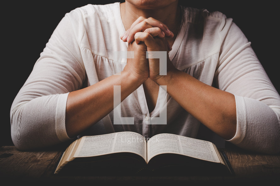 Woman with folded hands praying with open Bible
