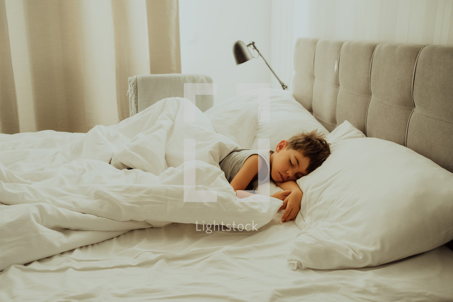 Calm little child sleeping well in comfortable bed. Boy with happy face and smile in light cozy bedroom. Healthy resting in morning, enjoying dreaming. High quality photo