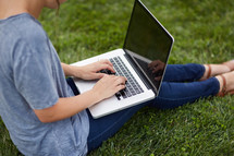a woman sitting in the grass with a laptop 