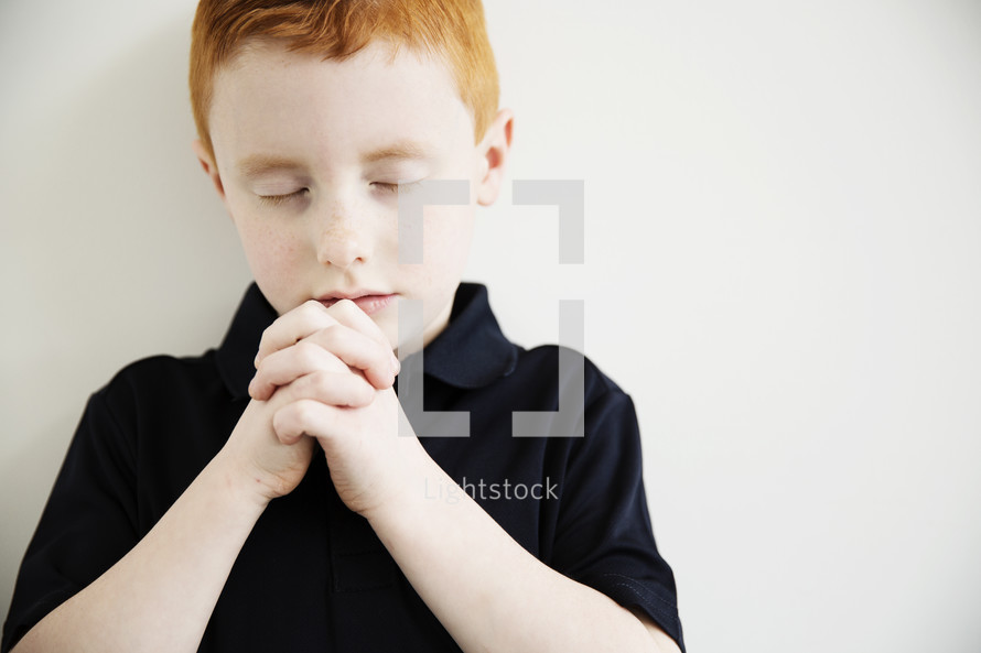 A little boy clasps his hands in prayer.