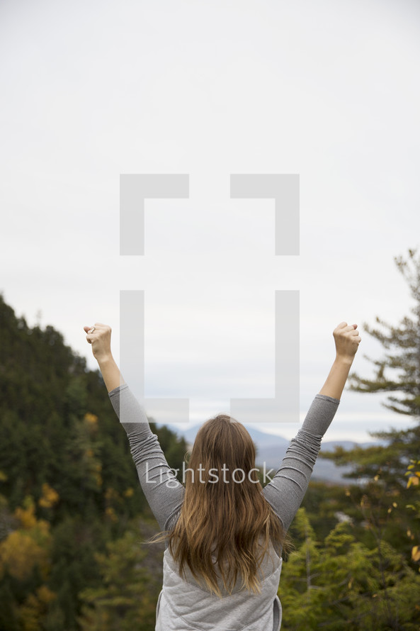 woman standing on a mountain with raised arms in victory 