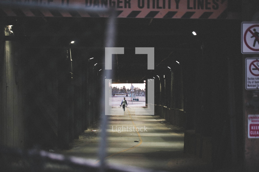 man walking under a bridge and a chain linked fence 