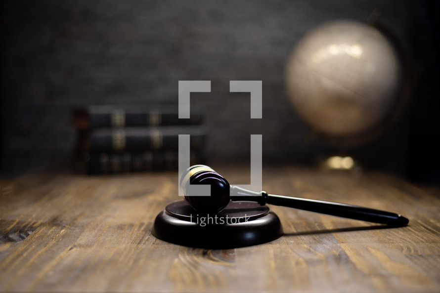 a gavel on a wooden table with bibles and globe in the background 