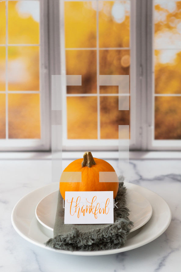 Thanksgiving place setting with the word thankful in front of a kitchen window