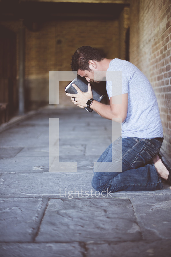a man kneeling in prayer holding a Bible 