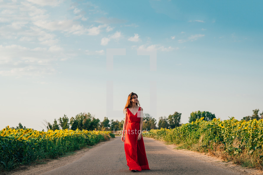 Woman with red dress walking on road with sunflowers.