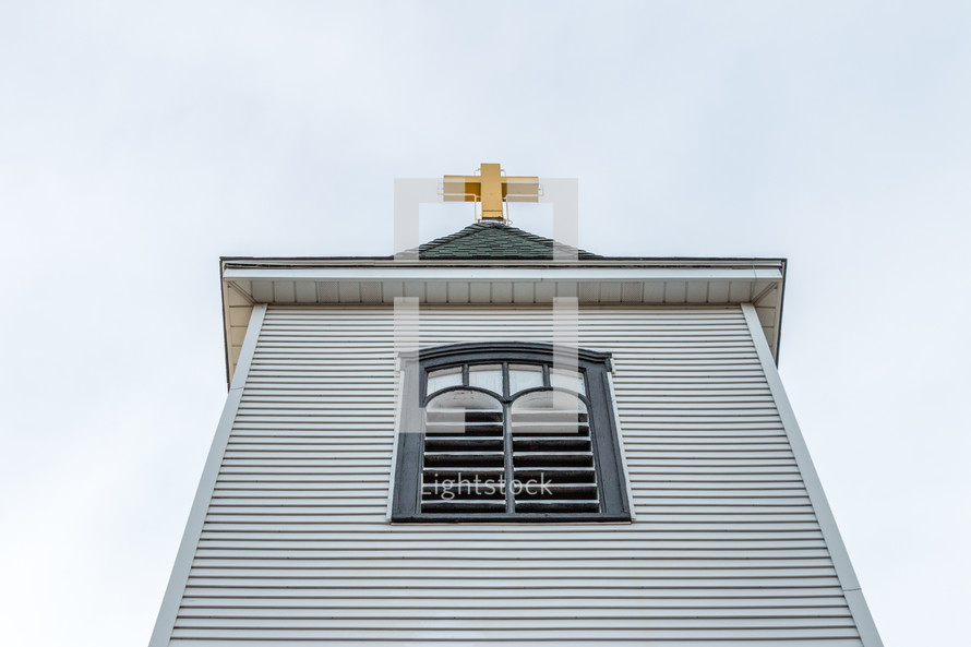Looking up at church steeple with golden cross on top