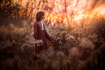 a girl standing in a field at sunset 