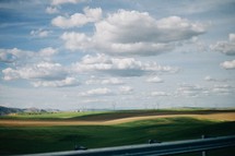 view of rolling hills and blue sky through a car window
