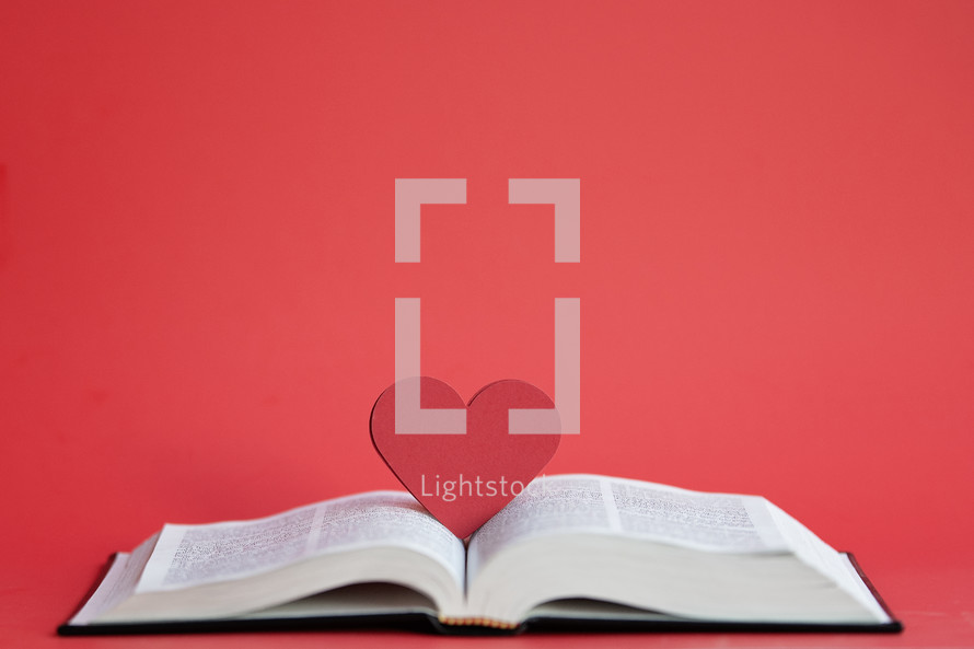 Close up red heart on an open Bible with a red background and copy space