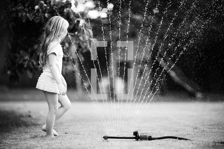 Girl playing in backyard water sprinkler during the summer.