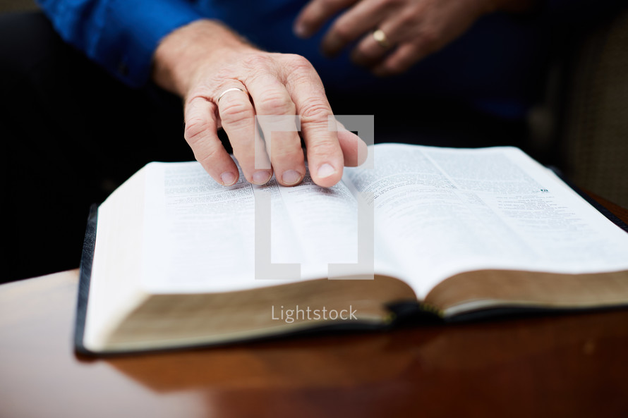 elderly man with hands on a Bible on a coffee table 