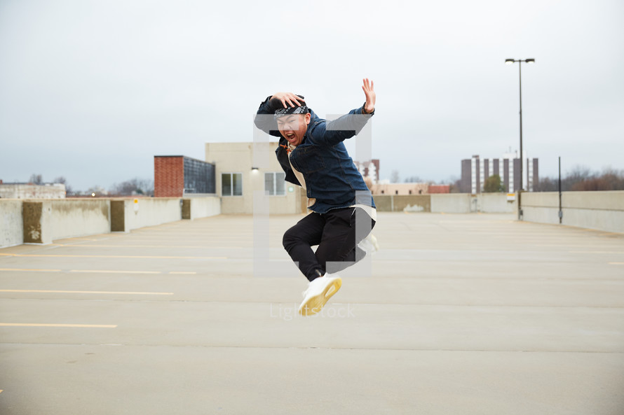 an Asian boy jumping up in a parking deck 