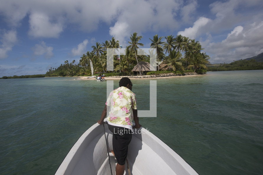 woman on the bow of a boat looking out at tropical water near and island