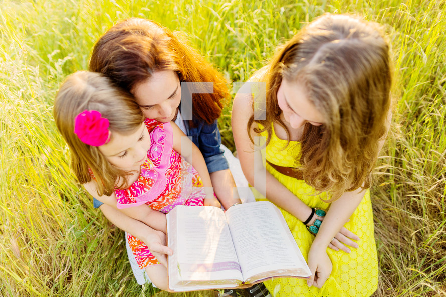 mother and daughters reading a Bible together outdoors