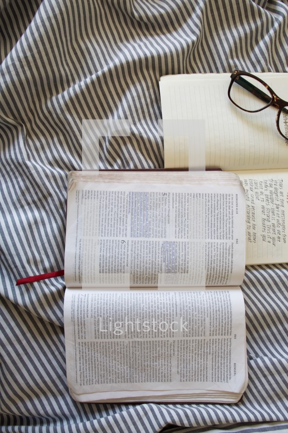 open Bible, reading glasses, and journal on a bed 
