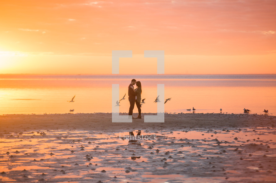 a couple hugging on a beach at sunset 
