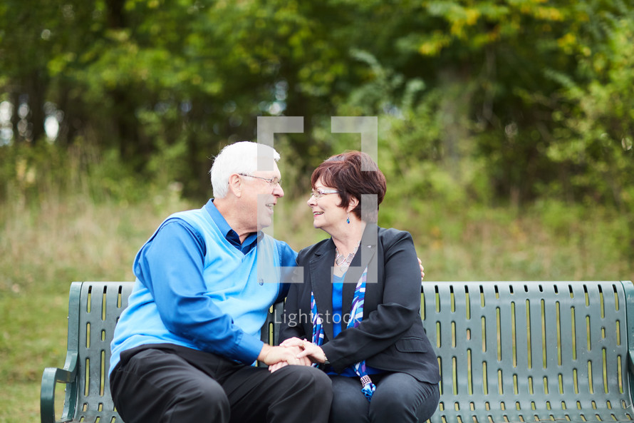 elderly couple sitting on a park bench 