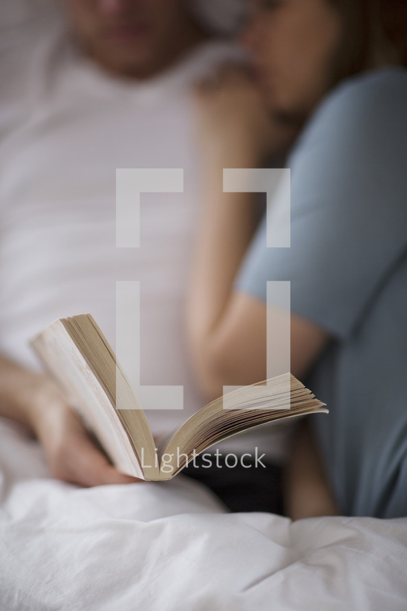 a couple lying in bed snuggling and reading a Bible 