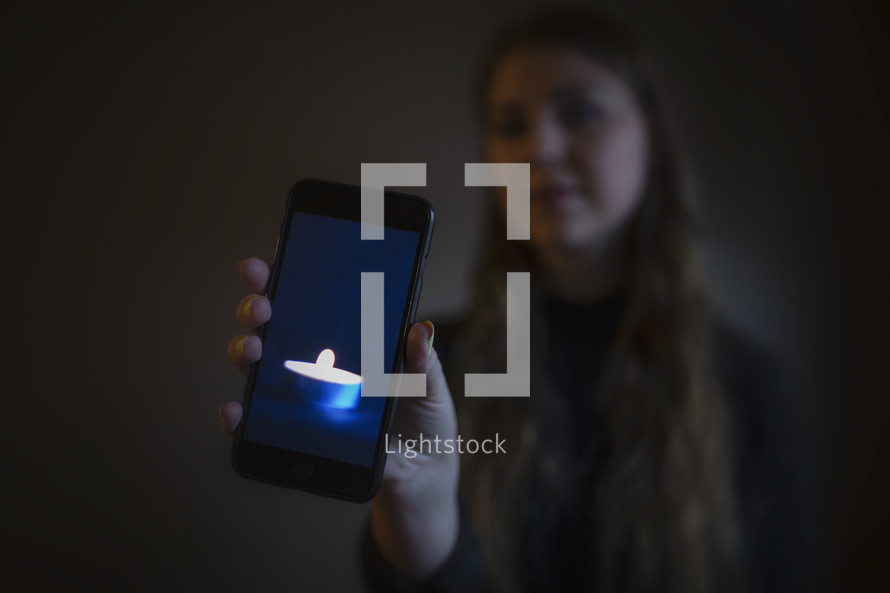 young woman holding image of candle burning in dark room