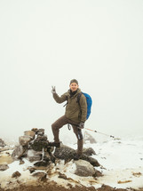 man showing a peace sign standing on a snowy mountain 