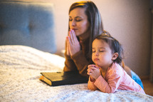 mother and daughter praying bedside 