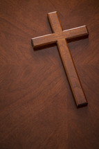 A mahogany wood cross on a similarly textured table top with copy space in lower left of frame 