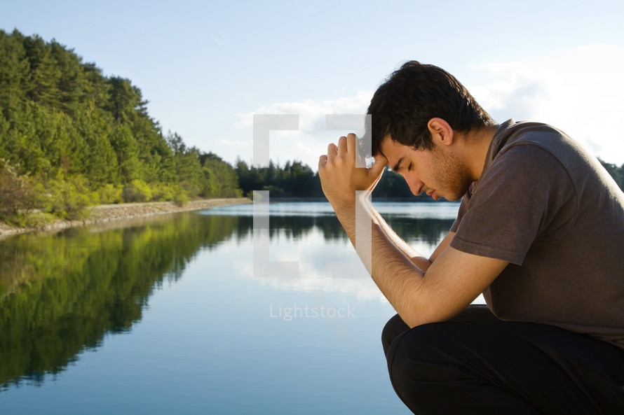 man praying by a lake