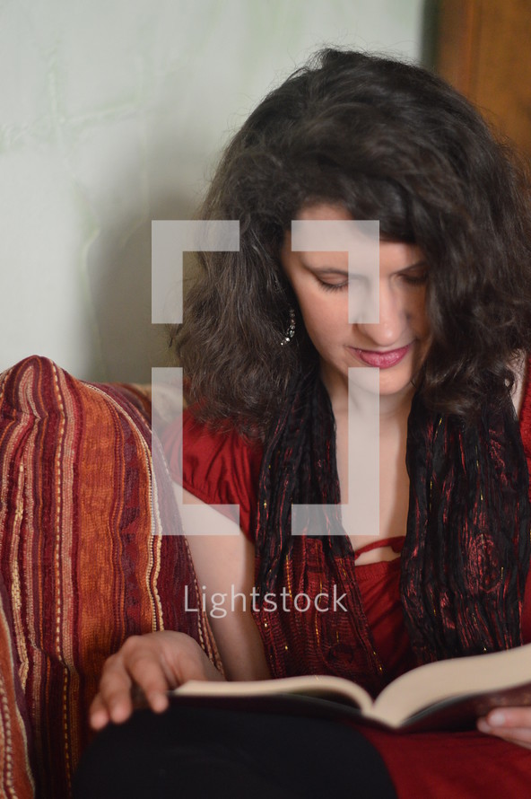 Woman reading the bible sitting on a red sofa