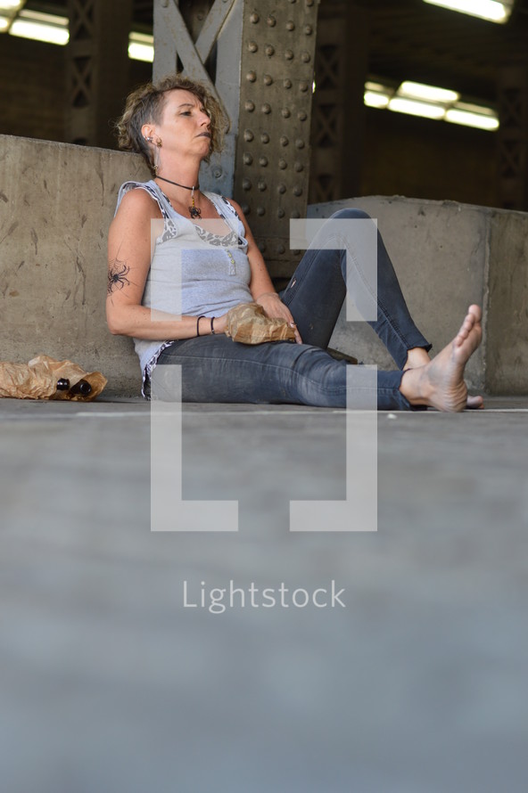 a woman under a bridge with bottles of alcohol 