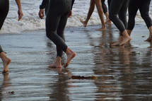 surfers in wetsuits walking on wet sand at the beach. 