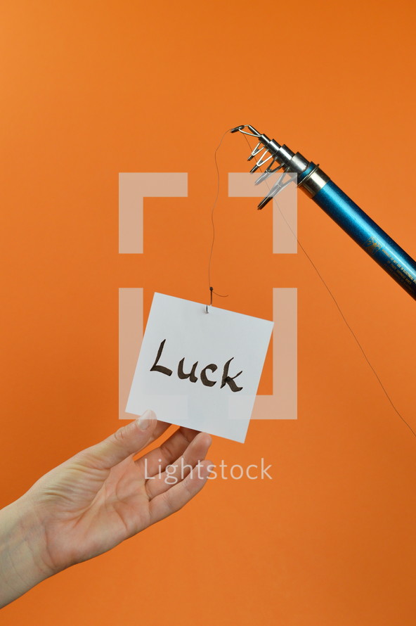 a hand grabbing for a piece of paper with the word LUCK on it hanging from a fishing line 